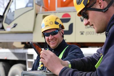 Twee mannen aan het werk in het verticaal transport, waarvan de een kijkt op een mobiel.Digitale werkopdrachten