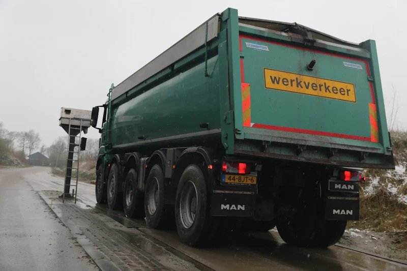 Groene MAN-dumptruck gezien van achteren op een natte weg; achterklep met 'werkverkeer', rode en gele reflecties, kenteken 44-BJT-6.