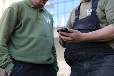 Twee groenvoorzieners kijken samen naar de mobiel van een van henMaar hoe krijg je dat voor elkaar, werken zonder papier?