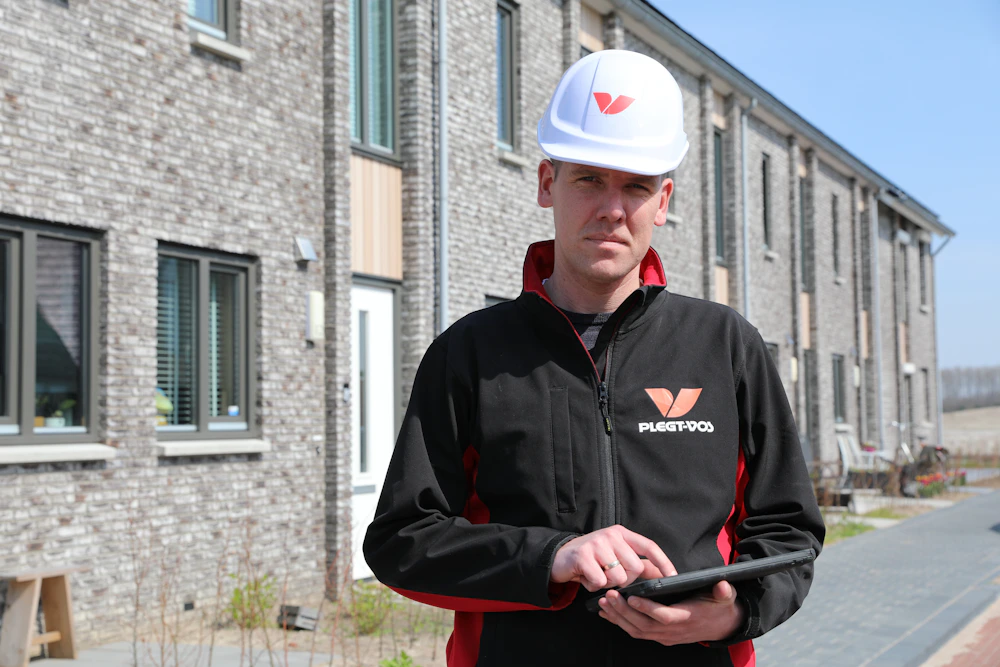 Bouwmedewerker met een witte bouwhelm op en een tablet in zijn handen.