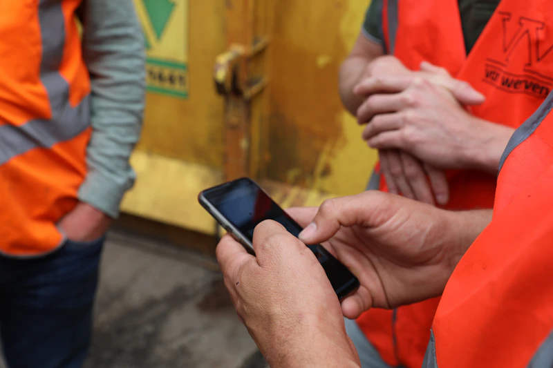 Drie medewerkers op de bouwplaats waarvan 1 een telefoon in handen heeft waar hij de BIM informatie op kan bekijken.