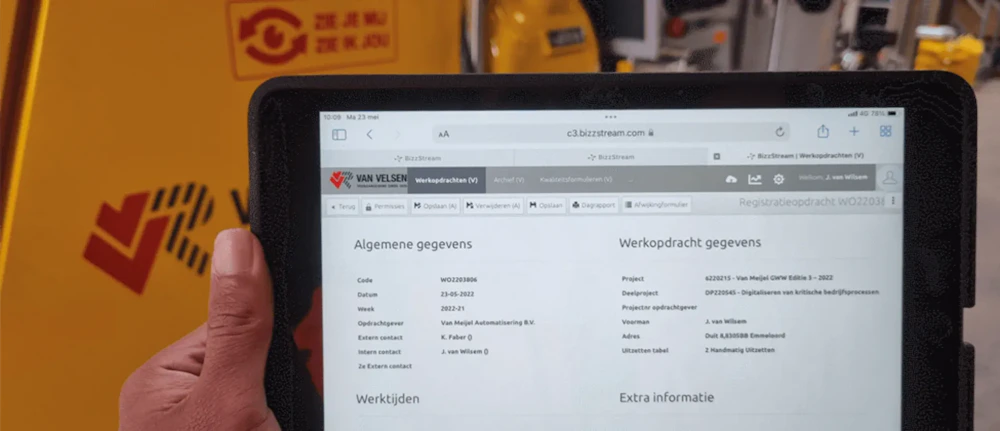 Persoon houdt een tablet vast naast een gele industriële machine; op het scherm staat een formulier met Algemene gegevens en Werkopdracht gegevens.